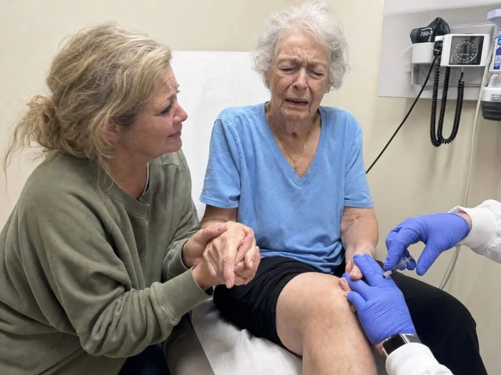 A woman gripping her swollen knee while sitting on an exam table